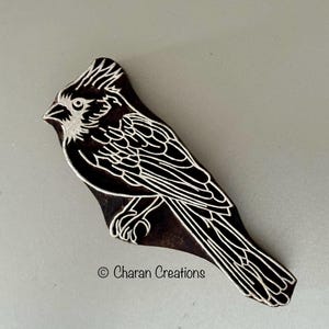 May include: A wooden block carving of a bird with white detailing. The bird is facing left and has a long tail. The carving is dark brown and has a smooth surface.