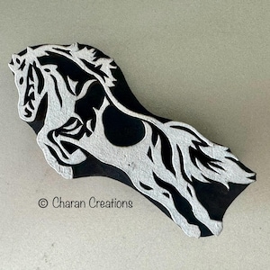 May include: A black and white wooden printing block featuring a carved design of a horse in motion. The horse is depicted with a flowing mane and tail. The text "© Charan Creations" is clearly visible in the lower left corner of the block.