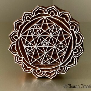 May include: A wooden block printing stamp with a detailed geometric design in white on a brown background. The design is a mandala with a flower-like border.