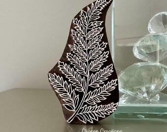 May include: A wooden block printing stamp featuring a detailed fern leaf design. The stamp is carved with a white fern leaf on a dark brown background.