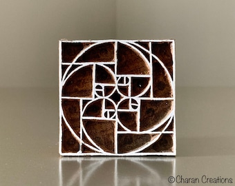 May include: A wooden printing block with a geometric design featuring a white spiral pattern on a brown background. The design is reminiscent of the Fibonacci sequence and the golden ratio.