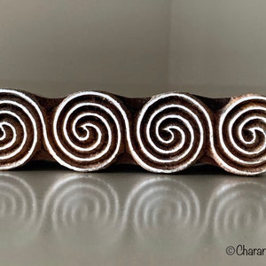 May include: A wooden printing block with four carved spiral designs. The block is brown with white spirals.