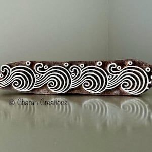 May include: A wooden printing block with a design of white waves with swirls on a brown background. The block is about 10 inches long and 1 inch wide.  © Charan Creations