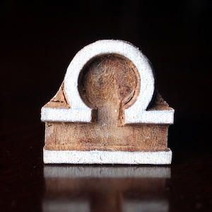 May include: A wooden zodiac sign for Libra, painted white with a brown wood grain showing through.