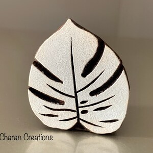 May include: White wooden block carved with a black monstera leaf design. This block is used for printing patterns onto fabric.