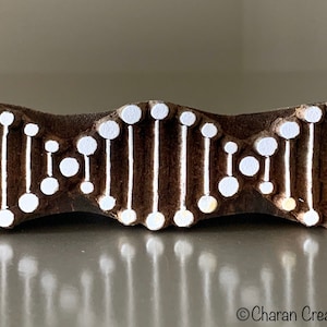Könnte beinhalten: Ein Holz-Druckblock mit einem weißen Design einer Doppelhelix, die an DNA erinnert. Der Block ist braun und hat eine leicht strukturierte Oberfläche.