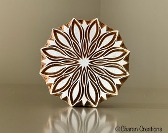 May include: A wooden block printing stamp with a detailed, intricate design of a flower with white and brown petals. The stamp is round and has a slightly raised edge.