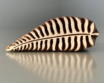 May include: A wooden block with a leaf design. The block is brown with white accents, featuring a detailed fern-like pattern. The block is approximately 13 cm long and is likely used for printing or stamping.
