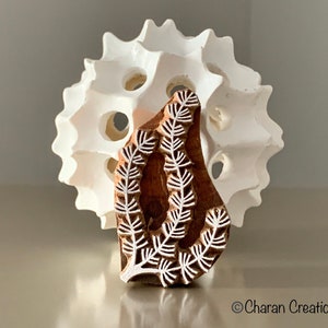 May include: A wooden block printing stamp with a white design of a leafy branch. The stamp is brown and has a natural wood grain.