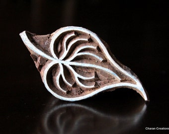 May include: A wooden block printing stamp shaped like a leaf with a detailed design carved into it. The leaf is outlined in white and has a brown wood grain.