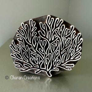 May include: A dark brown wooden block featuring a white coral design. The block has a hexagonal shape. The white coral design is detailed and covers the entire surface. The text "© Charan Creations" is at the bottom.