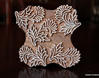 May include: A wooden block with a floral design carved into its surface. The design features stylized leaves and flowers with white outlines against a brown background. The block is likely used for printing or stamping.