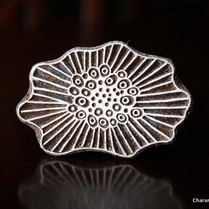 May include: A wooden block printing stamp with a floral design. The stamp features a central pattern of concentric circles surrounded by radiating lines. The stamp is brown with white detailing and has a scalloped edge.