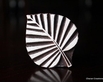 May include: A wooden block printing stamp shaped like a leaf with white and brown stripes. The stamp is used for creating patterns on fabric.