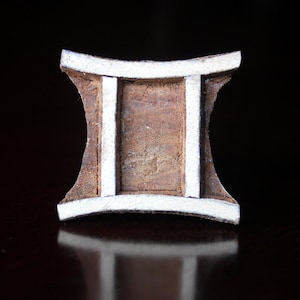 Op de afbeelding: Een houten sterrenbeeld voor Tweelingen, met een witte geverfde rand en een bruine houten kern.