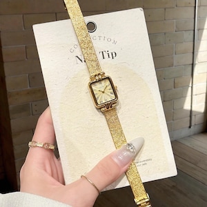 May include: Gold-toned wristwatch with a rectangular face and a mesh band. The watch face has Roman numerals and hands. The watch is displayed on a white card with the text "CTION Tip".