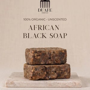 Puede incluir: Dos barras apiladas de jabón negro africano, con un aspecto áspero y texturizado, presentadas sobre una superficie con efecto mármol. El jabón es de color marrón oscuro. El texto "DUAFE ESSENCE" y "100% ORGANIC UNSCENTED AFRICAN BLACK SOAP" está incluido.