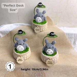 May include: Crocheted Totoro figures in beige pots with green 'grass' and a black soot sprite on a leaf. Each figure has a wooden tag with a message. Height is 3.94 inches.