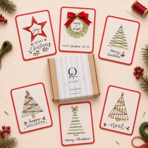May include: A DIY kit box with a blue and white striped label featuring the letter Q and the text DIY KIT, surrounded by five rectangular greeting cards with embroidered Christmas designs including stars, wreaths, and trees with red and green thread.