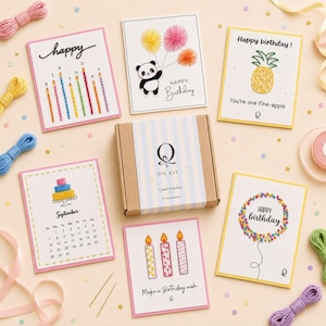 May include: A DIY kit box with a blue and white striped label featuring the letter Q, surrounded by six greeting cards with embroidered designs including a panda, a pineapple, a cake calendar, and candles, alongside colourful embroidery thread.