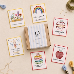Könnte beinhalten: Ein DIY-Set in einem Pappkarton mit blau-weiß gestreiftem Band, umgeben von fünf bestickten Karten mit lehrerspezifischen Motiven wie Blumen, einem Regenbogenstift, Äpfeln, einer Rakete und Büchern mit verschiedenen Texten wie Miss Sofia.