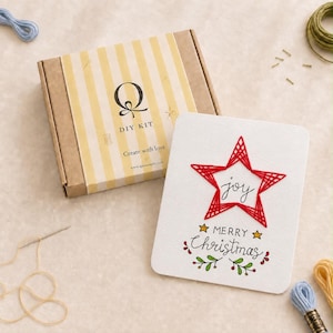 Könnte beinhalten: Ein DIY-Set in einem Karton mit gelben Streifen und dem Text Q DIY KIT Create with love, neben einer weißen Karte mit einem roten Stern aus Fadenkunst, dem Wort joy und dem Text MERRY Christmas mit kleinen grünen und roten Blattmotiven.