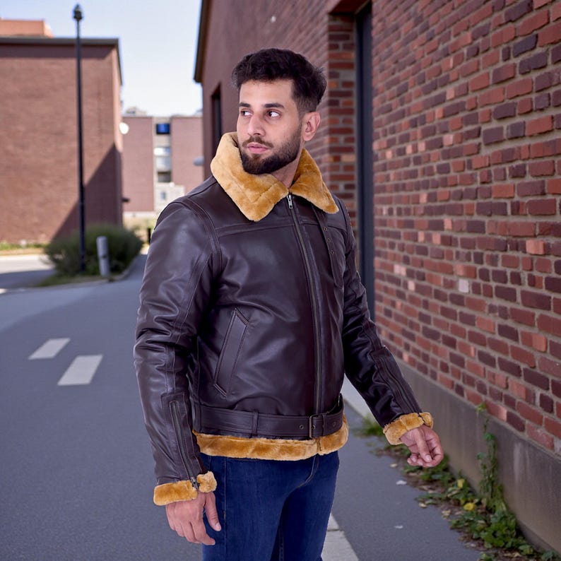 May include: A brown leather jacket with a tan fur collar and cuffs. The jacket has a zipper closure and a belt at the waist. The person is wearing blue jeans. The jacket is a classic style.