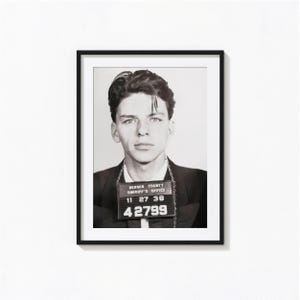 May include: A black and white framed portrait of a young person in a suit, holding a Bergen Sheriff's Office booking sign with the text 11 27 38 and 42799. The subject has dark hair and is wearing a dark jacket over a light collared shirt.