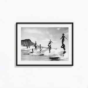 May include: A black and white framed photograph depicting multiple surfers riding waves in the ocean. Some surfers are standing on boards, while others are performing stunts like carrying another person on their shoulders near a mountain.