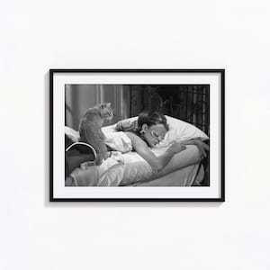 Könnte beinhalten: Ein schwarz-weiß gerahmtes Foto, das eine Person im Bett mit einer Schlafmaske zeigt, während eine Katze auf der Bettdecke in der Nähe sitzt. Die Szene umfasst Kissen und ein Kopfteil, festgehalten in einem klassischen, kontrastreichen Filmstil.
