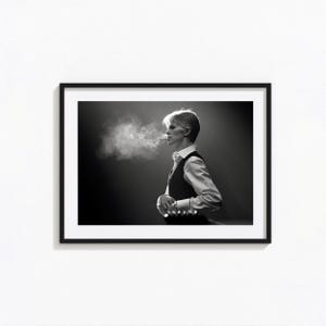 Könnte beinhalten: Ein schwarz-weißer gerahmter Fotodruck, der das Seitenprofil von David Bowie in einem hellen Hemd und einer dunklen Weste zeigt. Die Person atmet eine Rauchwolke aus und blickt in einer schwach beleuchteten Umgebung nach vorne.