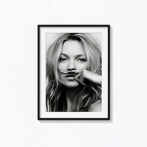May include: A black and white framed portrait print featuring a person with long hair holding a finger horizontally across their upper lip. The finger displays a small, dark, mustache-shaped graphic, creating the appearance of a mustache.