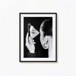 May include: A black and white framed wall art print featuring a side profile of a person holding a jagged shard of a mirror. The reflection in the glass shows a single eye. The person wears a large hoop earring and a dark textured jumper.