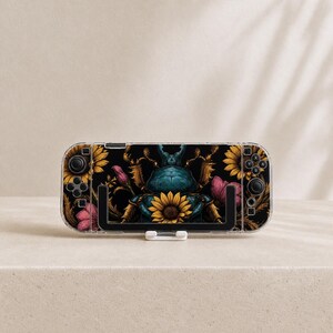 May include: A handheld gaming console featuring a black skin with a central blue beetle illustration surrounded by yellow sunflowers and pink floral accents. The device includes standard black control buttons, joysticks, and a directional pad.