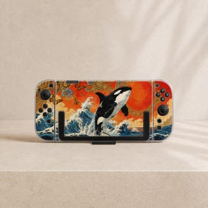 May include: A handheld gaming console featuring a decorative skin with an orca jumping out of blue ocean waves against a vibrant orange background. The design includes intricate gold circular patterns and small butterflies across the surface.