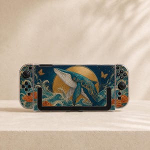 May include: A handheld gaming console featuring a protective case with a dark blue background, a large golden moon, and a central blue whale illustration. The design includes stylized ocean waves, orange floral accents, and small golden butterflies.