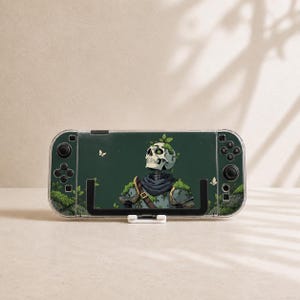 May include: A handheld gaming console featuring a dark green skin with an illustration of a skeleton wearing armor covered in moss and small green leaves. The design includes small white butterflies against a dark green background.