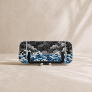 May include: A handheld gaming console featuring a clear protective case with a printed design of dark grey swirling clouds above turbulent blue ocean waves. The device includes black control buttons, joysticks, and a black stand on the front.
