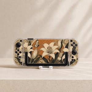 Peut inclure: Une console de jeu portable dotée d'une coque de protection transparente sur un habillage illustré de lys couleur crème, de feuillage vert foncé et d'un petit papillon sur un fond circulaire texturé aux tons orange chaud et doré.