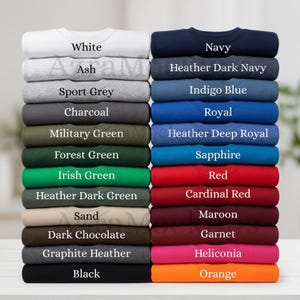 May include: A stack of folded crew neck sweatshirts in various colors, including white, navy, gray, green, red, and orange. Each shirt is labeled with its color name, such as "White," "Navy," and "Orange."