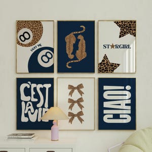 May include: Six framed art prints with gold frames. The prints feature various designs, including an 8-ball with leopard print, two leopards, star with leopard print, bows, and the phrases "LUCKY ME", "STARGIRL", "C'EST LA VIE", and "CIAO!".
