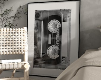 May include: Monochrome framed print featuring a cassette tape. The tape, with the text "POSITION CHRO" and "90", is centrally positioned within a black frame. The print is displayed in a room with a chair and a neutral colour scheme.