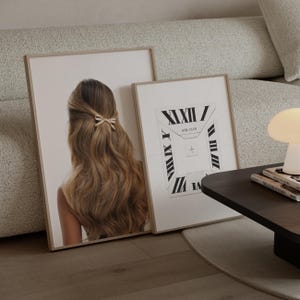 May include: Two framed art prints. One shows a woman's long, wavy, light brown hair with a bow. The other print has a black and white design with Roman numerals and the text "GIRL CLUB". Both are in light wood frames.