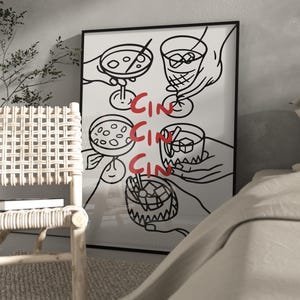 Puede incluir: Lámina artística enmarcada en negro con una ilustración minimalista de manos sosteniendo cócteles. La palabra "CIN" está escrita en rojo en la imagen. La obra de arte se exhibe en una habitación con una silla de mimbre y una cama.