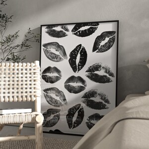 Puede incluir: Una impresión artística enmarcada con múltiples marcas de besos de lápiz labial negro sobre un fondo blanco. Las huellas de labios varían en tamaño y orientación, creando un patrón. La obra de arte se muestra en un marco negro.