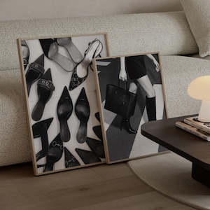 May include: Two framed black and white art prints. One features an arrangement of various high-heeled shoes. The other depicts a person holding a black handbag, wearing a black dress and boots, walking on a crosswalk.