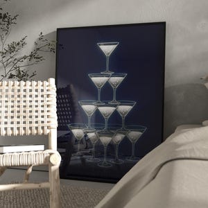 Peut inclure: Une affiche encadrée représentant une pyramide de verres à martini remplis d'un liquide pétillant, sur fond bleu foncé. L'œuvre est exposée dans une pièce avec une chaise en osier et un lit.