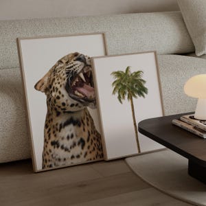 May include: Two framed art prints. One depicts a roaring leopard with visible teeth and spots. The other shows a palm tree against a white background. Both are in light wood frames, suitable for home decor.