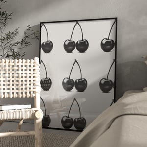 Puede incluir: Lámina enmarcada en blanco y negro con nueve cerezas. Las cerezas se muestran en varias disposiciones, algunas individuales y otras en pares, con tallos. La obra de arte se exhibe en un entorno interior moderno.