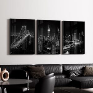 Puede incluir: Un conjunto de tres impresiones enmarcadas en blanco y negro de paisajes urbanos. Las imágenes representan un puente, un paisaje urbano con un edificio alto y una escena frente al mar con un barco. La obra de arte se exhibe sobre un sofá de cuero negro.